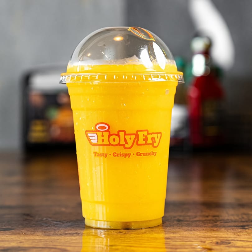 A Holy Fry branded cup filled with a bright yellow beverage, condensation on the outside.