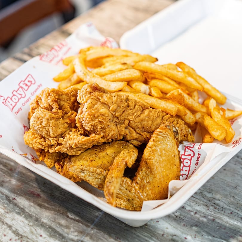 Crispy fried chicken pieces and golden french fries served in a white takeout container.