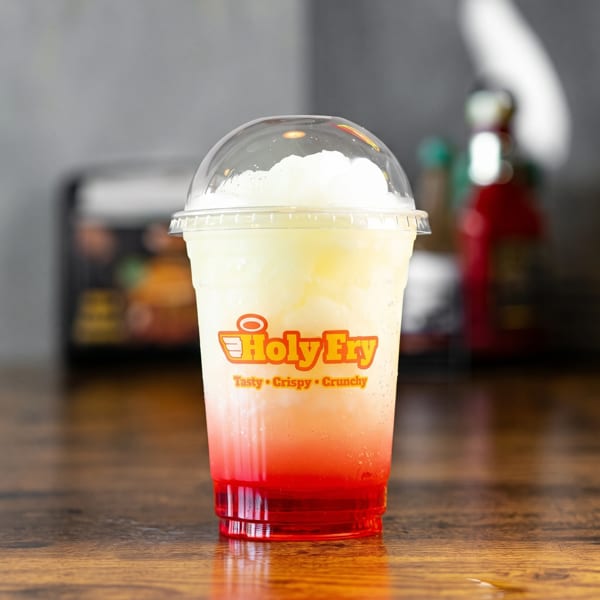 Holy Fry branded cup with a red and white layered slushy drink on a wooden table.