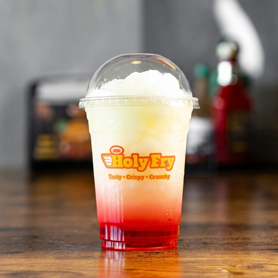 Holy Fry branded cup with a red and white layered slushy drink on a wooden table.