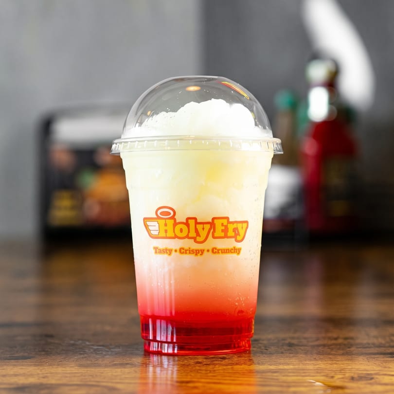 Holy Fry branded cup with a red and white layered slushy drink on a wooden table.