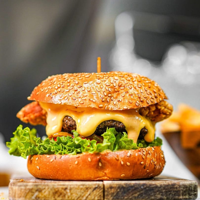 A juicy burger with melted cheese, fresh lettuce, and crispy fried chicken on a sesame seed bun.
