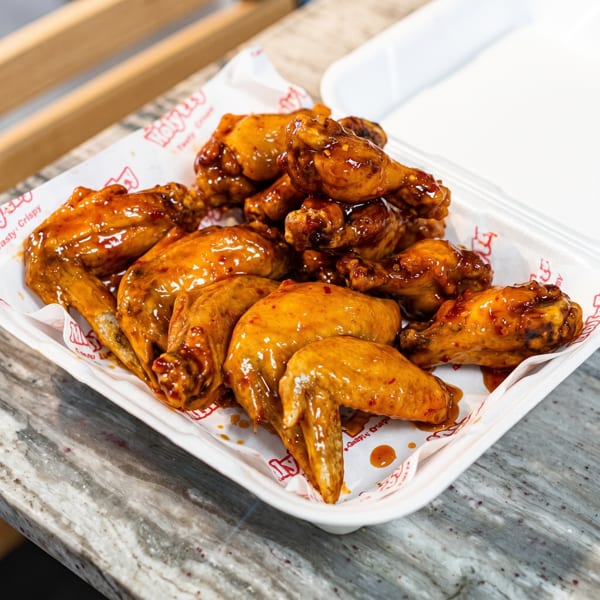 A white takeout container filled with glistening, saucy chicken wings on a marbled countertop.