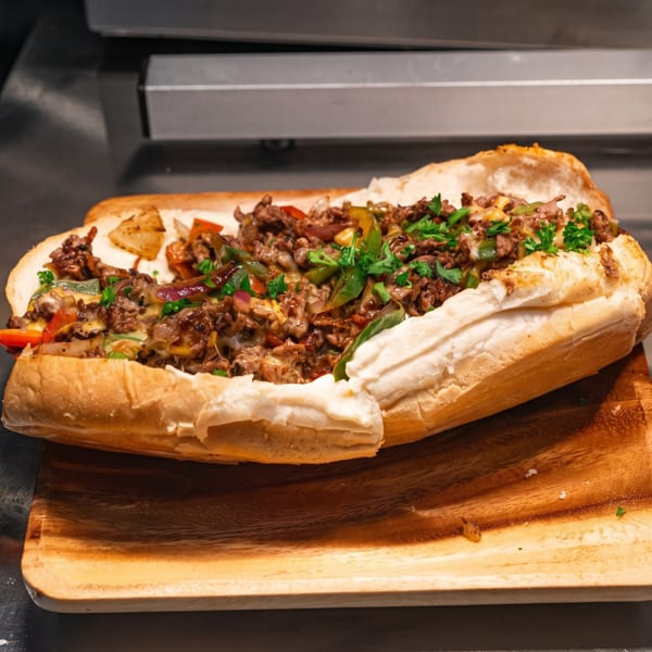 A close-up of a loaded cheesesteak sandwich with peppers, onions, and melted cheese on a wooden board.